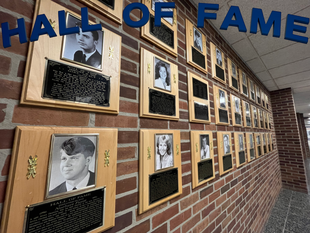 Plaques of past Attica Athletics Hall of Fame inductees are pictured hanging on a wall with the words "Hall of Fame" overlaid along the top edge of the image.